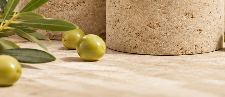ثمار زيتون أخضر وأغصان زيتون على سطح حجري فاتح